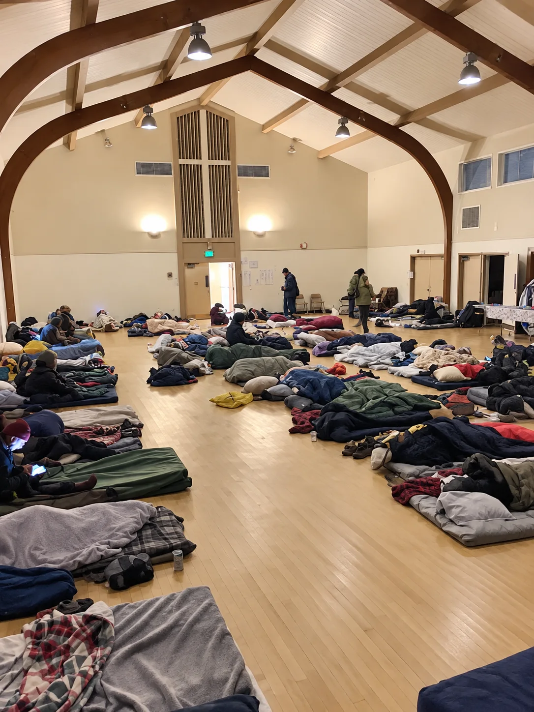 A warmly lit winter shelter room with sleeping spaces arranged across the floor.