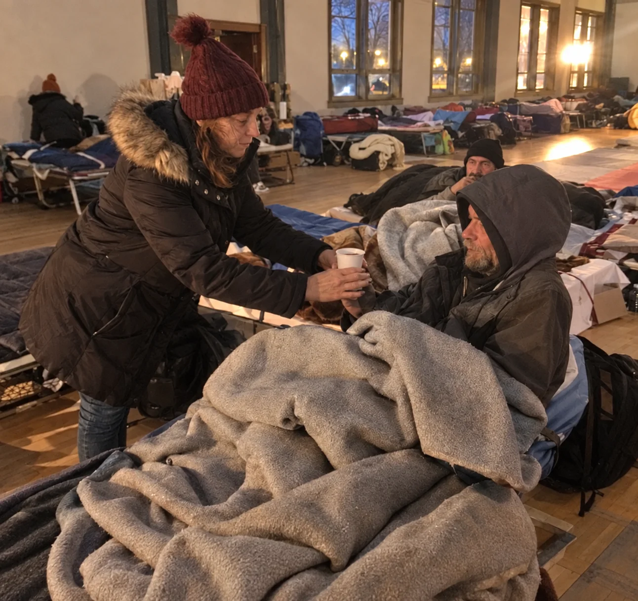 A volunteer offering a warm drink inside an overnight shelter.